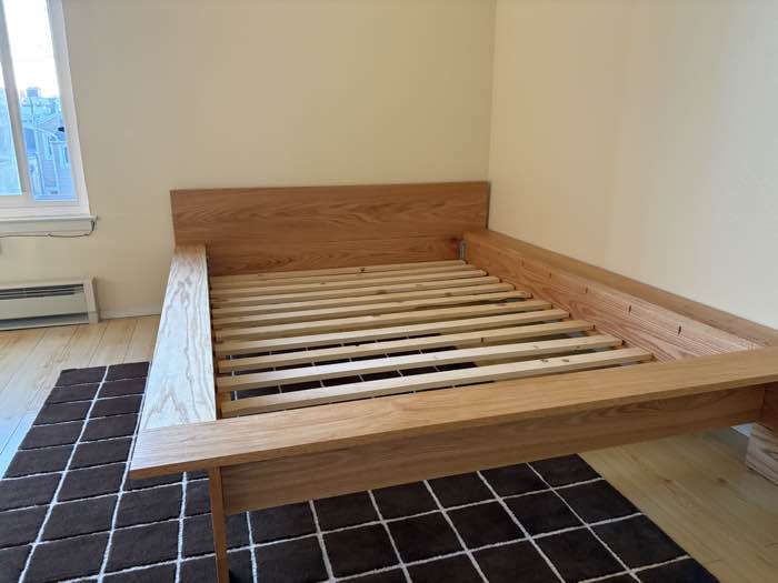 Oak platform bed frame with slats in an empty bedroom